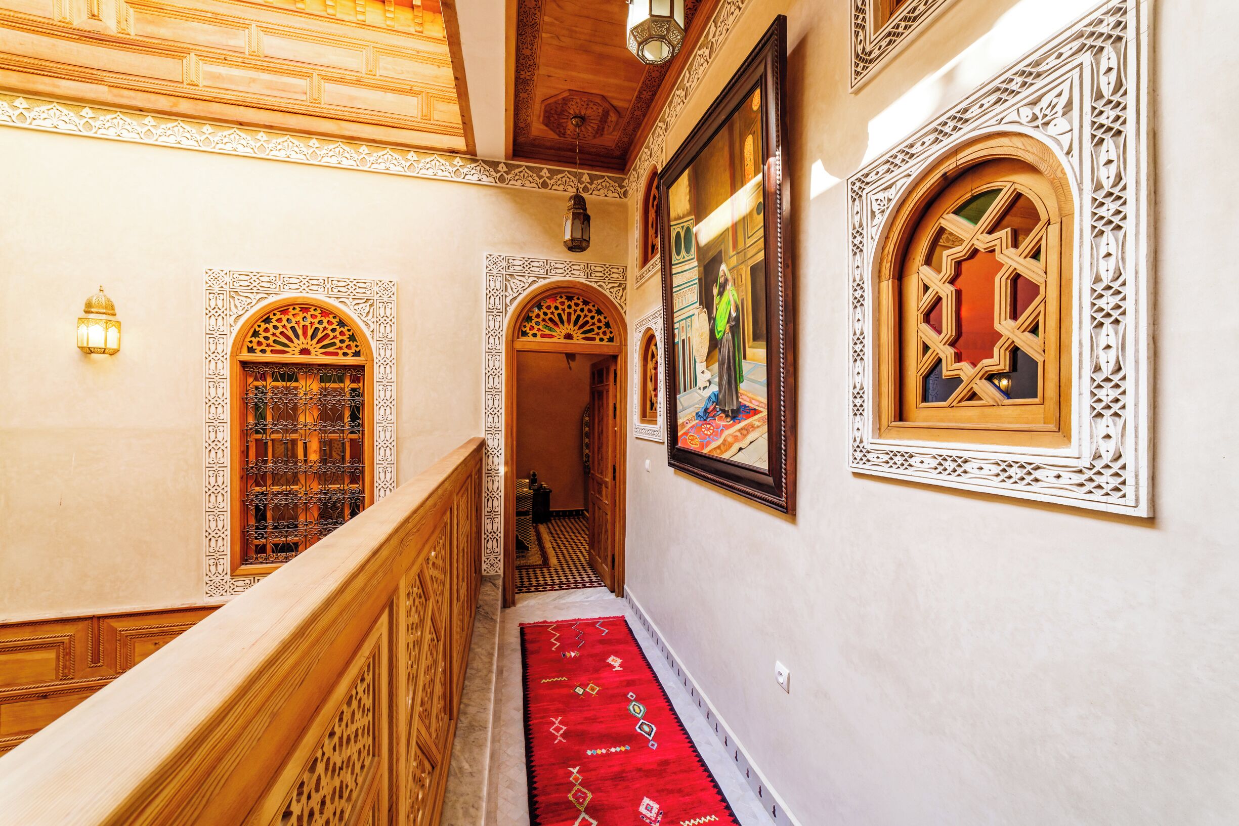 A hallway with ornate wooden railings, patterned rugs, and decorative wall panels.
