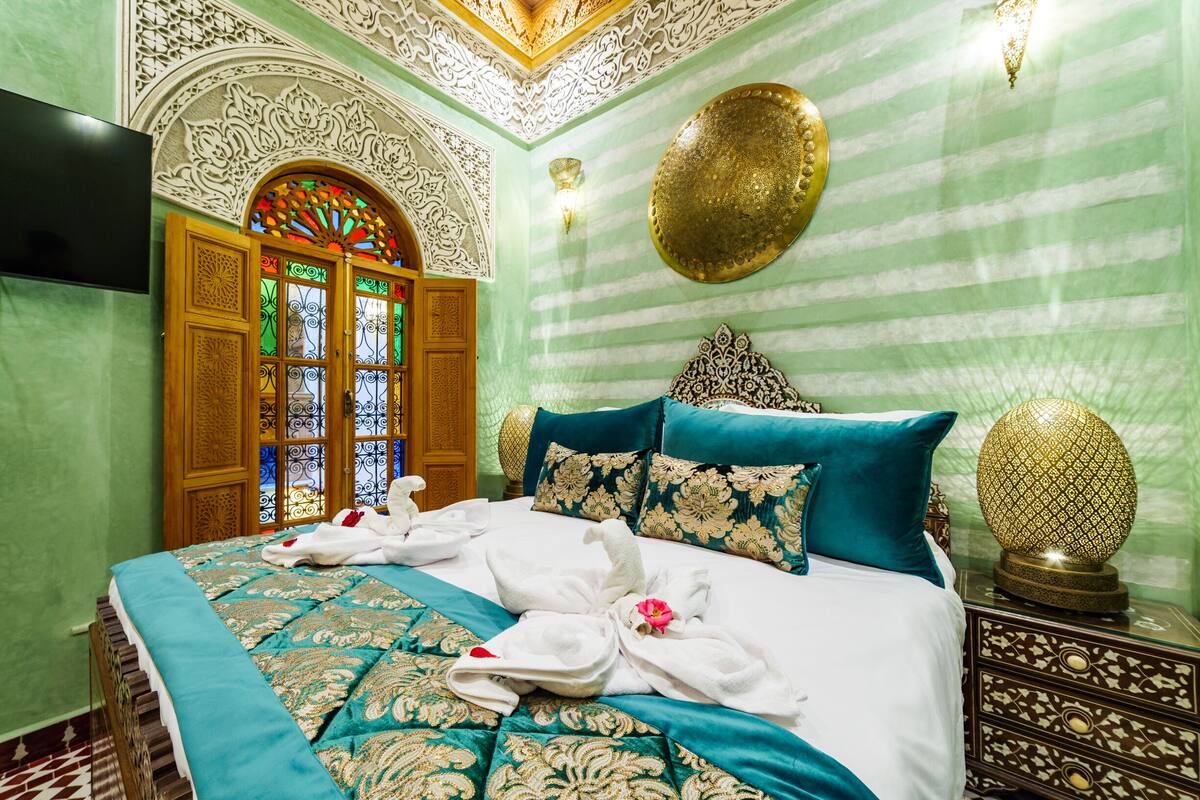 Quarto com cama, televisão, parede decorativa e porta com vitrais.