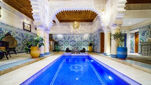 Una piscina con elaborados diseños de mosaicos, rodeada de columnas ornamentadas y detalladas decoraciones en las paredes.