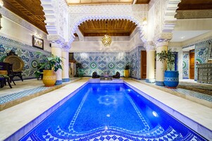 Uma piscina com trabalhos em azulejos elaborados, rodeada por colunas ornamentadas e detalhes decorativos nas paredes.