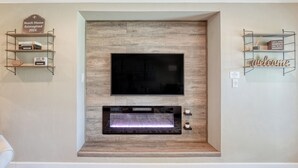Uma sala de estar moderna com uma TV de tela plana fixada em uma parede de madeira, uma lareira embutida e duas estantes de metal com objetos decorativos.