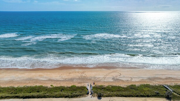 Uma praia com vista clara para o oceano, uma faixa de areia e algumas pessoas caminhando.