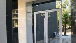 Une entrée moderne avec une porte en verre, un petit espace extérieur aménagé avec des sièges et un sol carrelé.