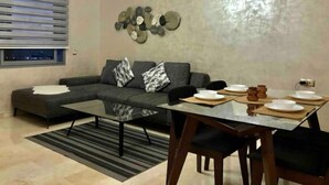 Un salon moderne avec un canapé d’angle, une table à manger avec des chaises et un élément décoratif mural.