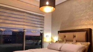Une chambre avec un grand lit, une fenêtre avec des stores et un luminaire suspendu.
