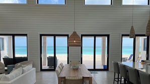 A spacious living area with a large wooden table, comfortable seating, and a view of the beach through glass doors. - Steps From the Water on One of The Most Beautiful Beaches in Exuma! (Rokers Point Settlement)