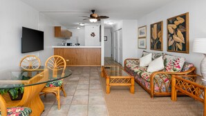 Ein modernes Wohnzimmer mit einem Glastisch, Korbmöbeln, einer Couch mit floralen Kissen und einem Deckenventilator.