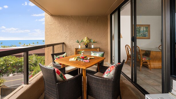 Ein Balkon mit Korbmöbeln, einem Holztisch und Blick auf den Ozean.