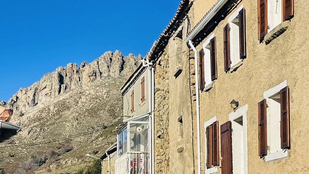 A stone building with a balcony, a staircase, and a mountain in the background. - Appartement Dans la Montagne (Albertacce)