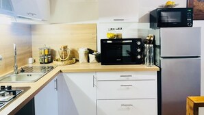 A modern kitchen with white cabinets, a microwave, a refrigerator, and a sink. - Appartement Dans la Montagne (Albertacce)