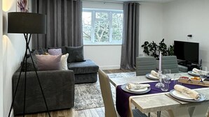 Un salon moderne avec un canapé, une table à manger dressée pour deux personnes et un téléviseur.