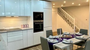 Une cuisine moderne avec des meubles blancs, un four encastré et un coin repas avec une table dressée pour quatre personnes.