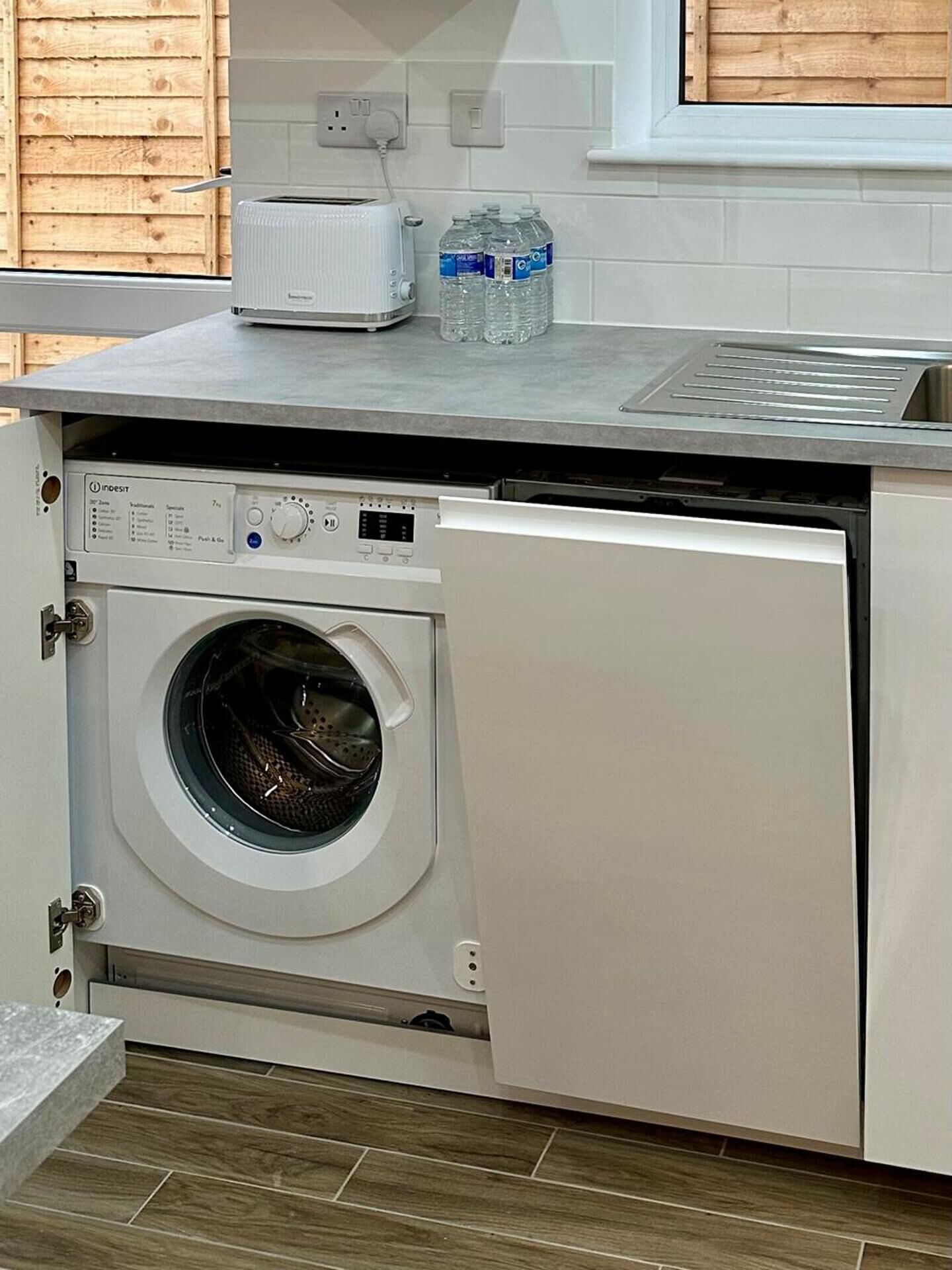 A compact laundry area with a front-loading washing machine, a small countertop, and a window above the sink.