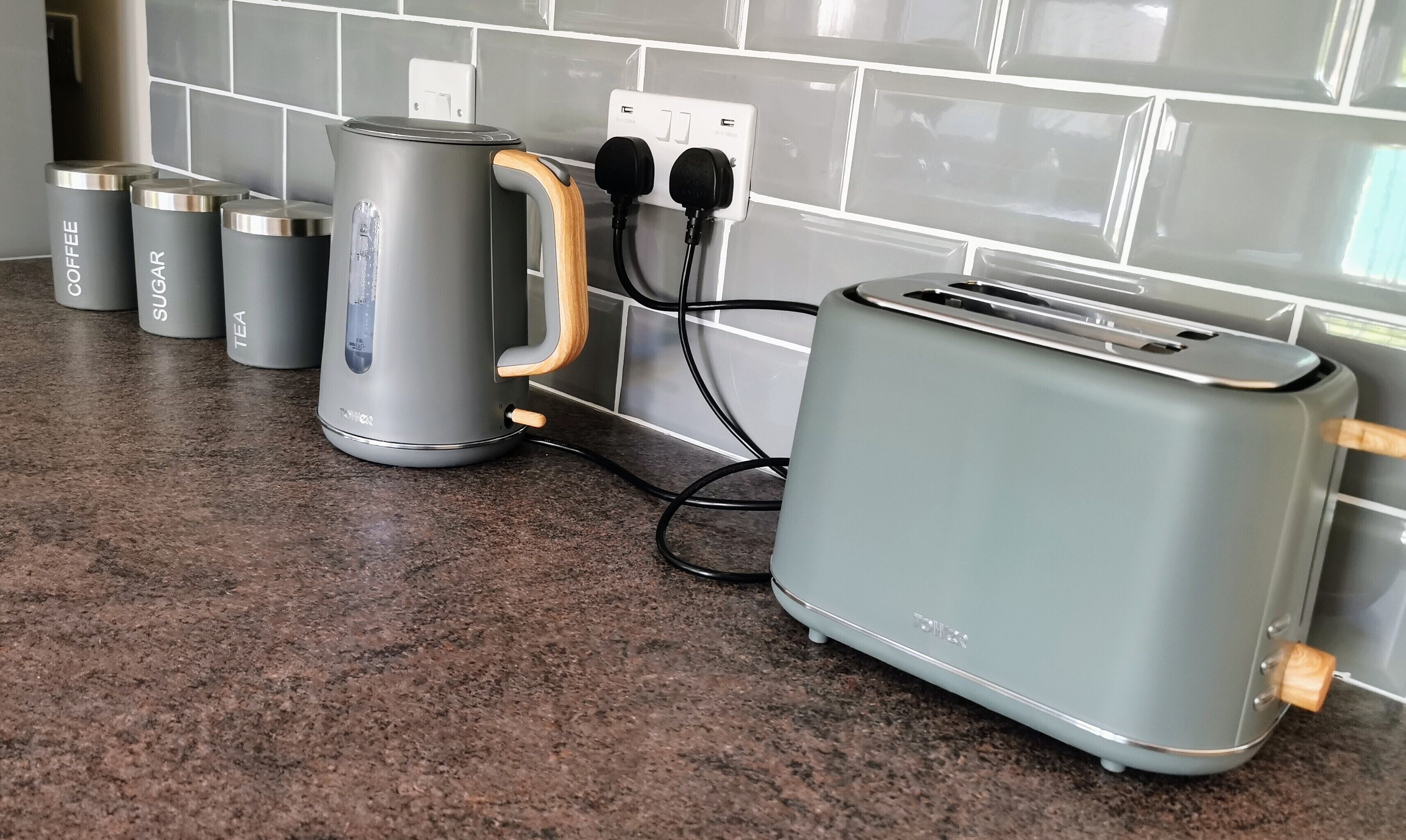 A kitchen with a toaster, kettle, and three containers labeled coffee, sugar, and tea.