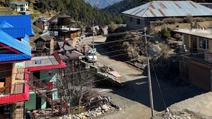 A mountainous village with traditional houses, a clear sky, and snow-capped peaks in the distance.
