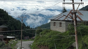A rural road with a white car, a small building with a brick wall, and a mountain range in the background. - Snow Mount View (Dalhousie)