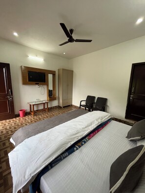 A hotel room with a bed, a desk, a chair, a television mounted on the wall, and a ceiling fan.
