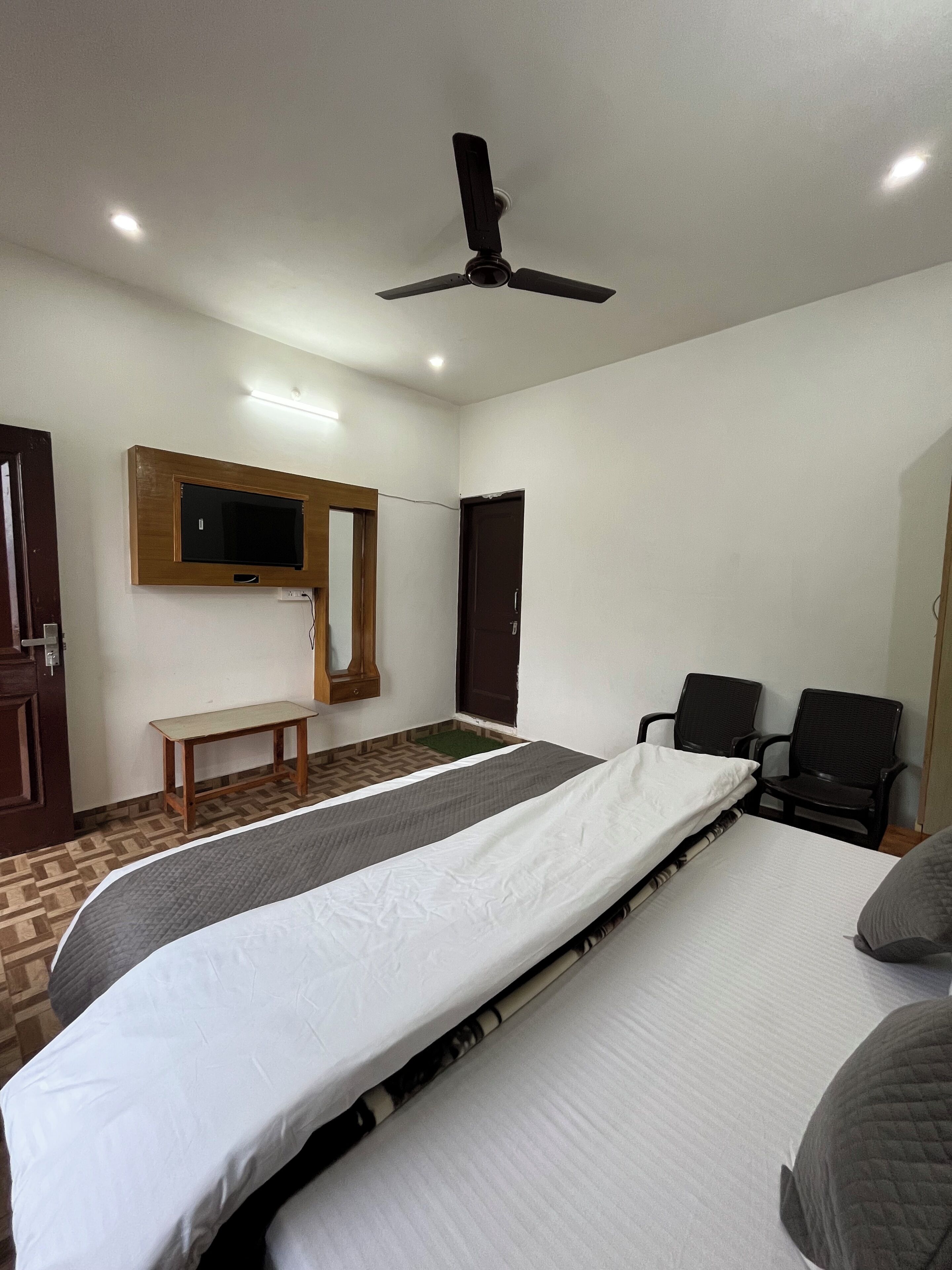 Un dormitorio con cama, dos sillas, un banco, televisor y ventilador de techo.