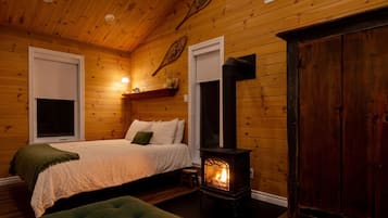 Une pièce chaleureuse, aménagée dans une cabane en bois, avec un lit, un fauteuil recouvert d’un tissu vert, un radiateur fixé au mur et une grande porte en bois.