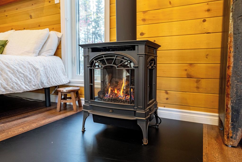 A wood-burning stove in a room with wooden walls and a bed.