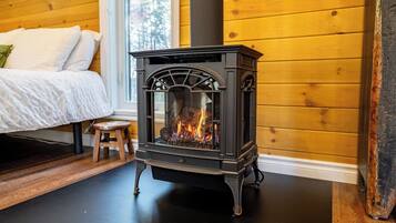 A wood-burning stove in a room with wooden walls and a bed.