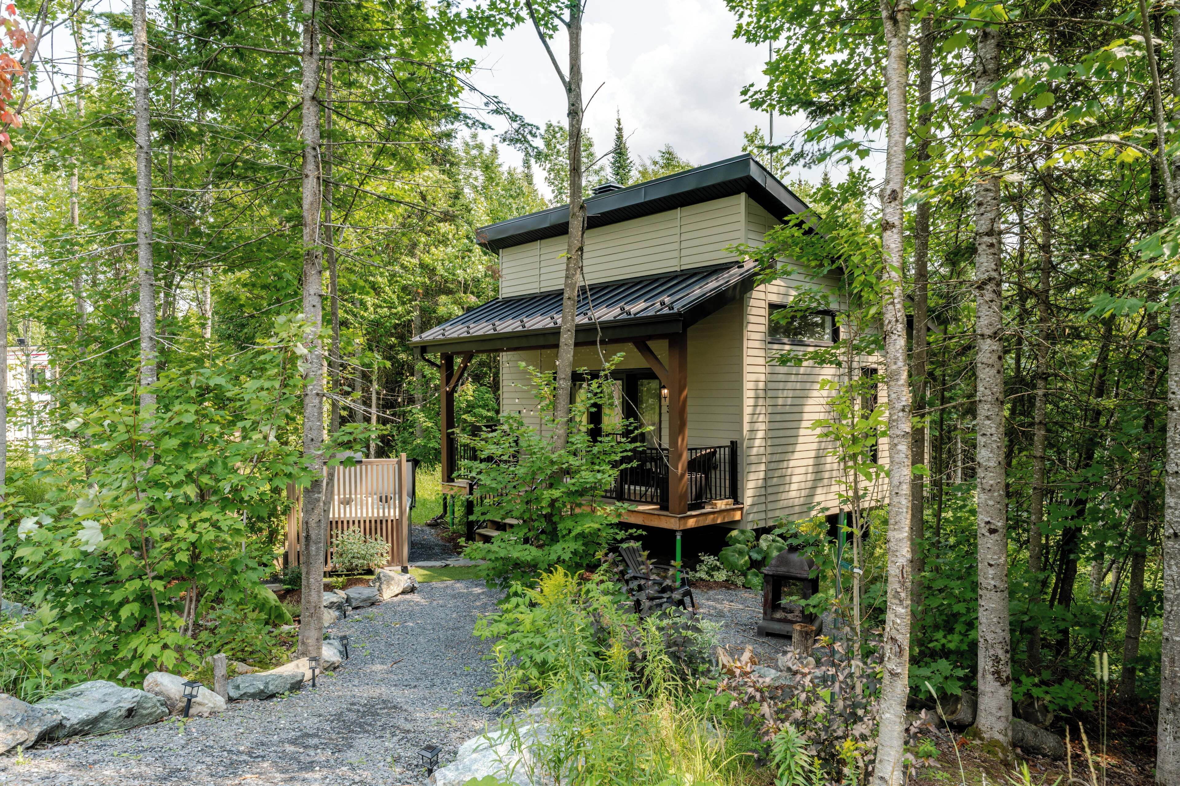 A cabin with a covered porch, surrounded by a forested area with a gravel path leading to the entrance.