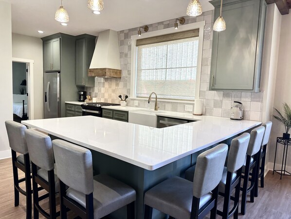 Una cocina moderna con una isla grande, taburetes de bar e iluminación colgante.