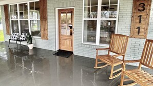 A covered porch with a brick wall, wooden rocking chairs, and a bench. - Luxury Home Near Crater of Diamonds 
3 King Beds 2 Full Baths
Sleeps 7 (Nashville)