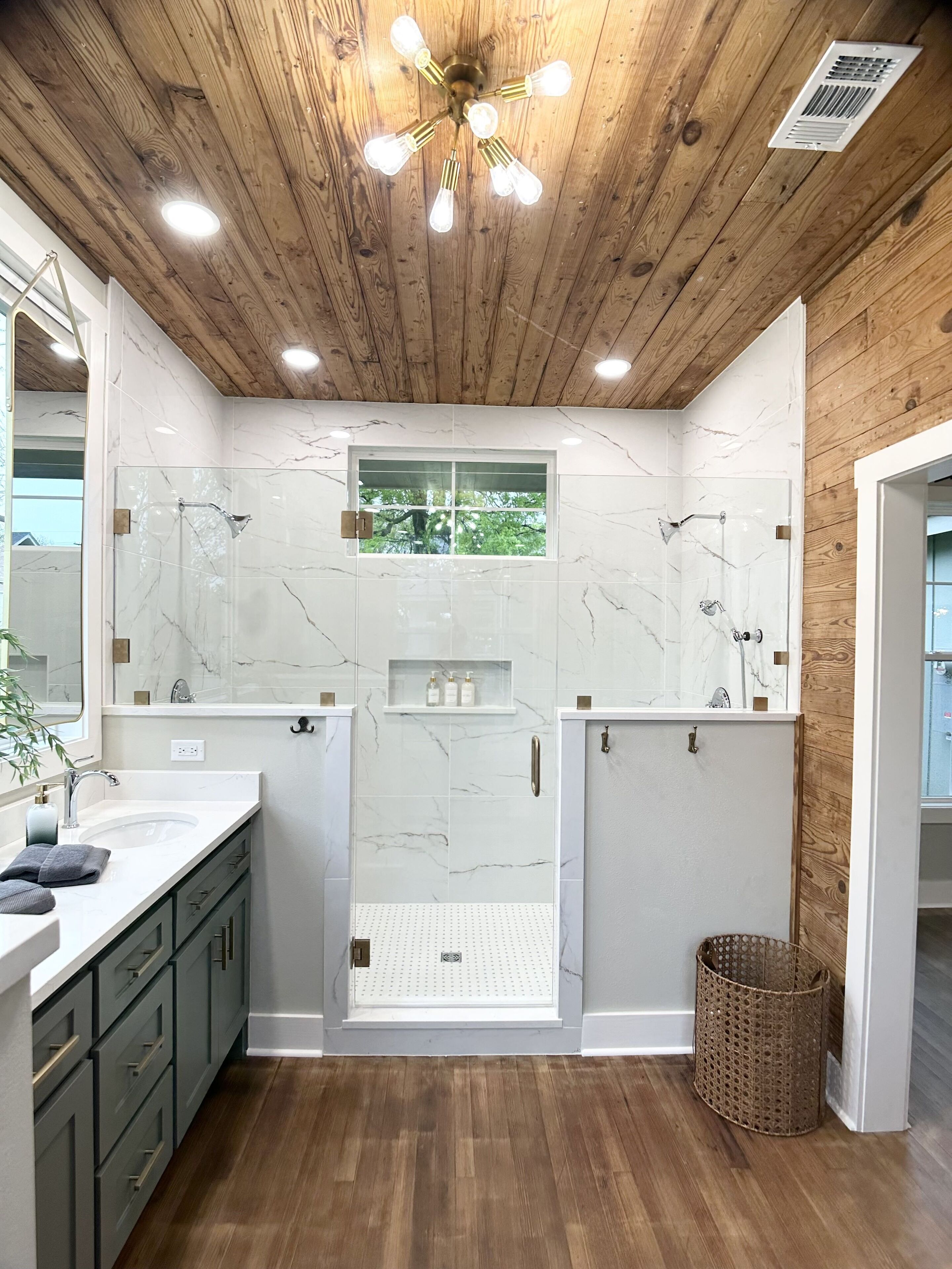 A modern bathroom with a wooden ceiling, a large mirror, a walk-in shower, and a sink with a wooden floor.