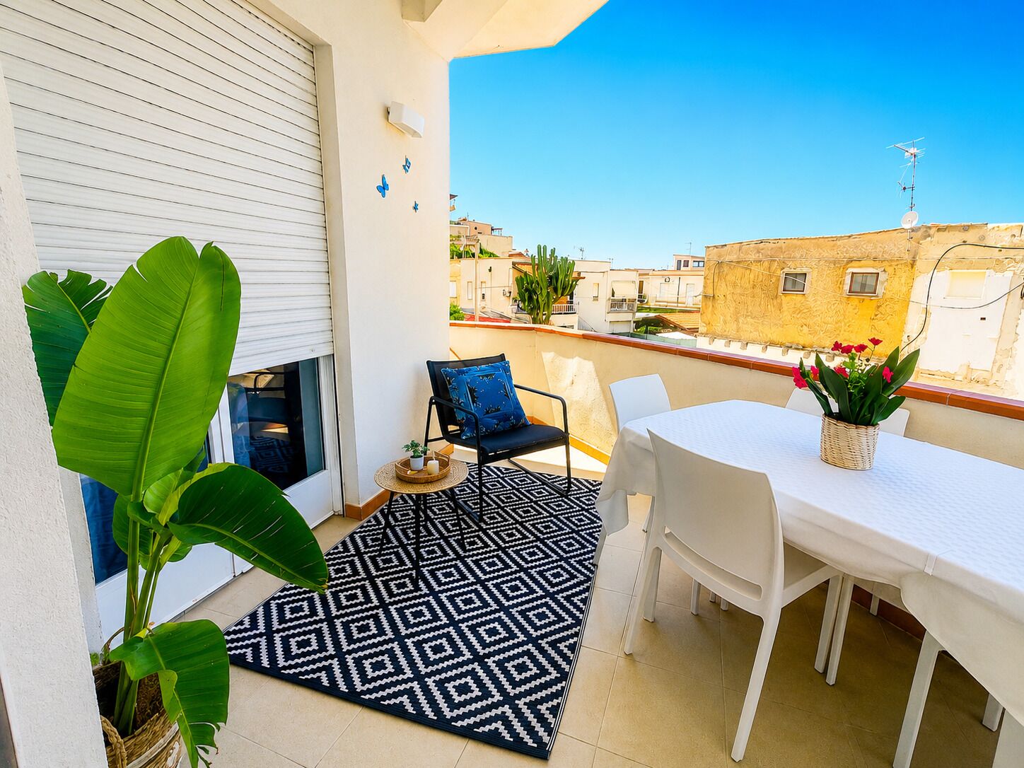 A balcony with a dining table, chairs, a patterned rug, and potted plants.