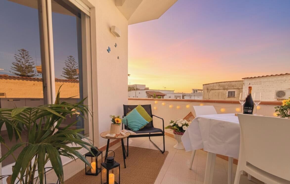 A balcony with a table set for two, a chair, a potted plant, and a bottle of wine.