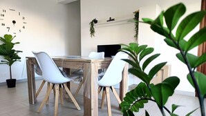 A dining area with a wooden table and white chairs, a black monitor on the table, and a wall clock. - Appartamenti Abate  Conchiglia Home  (Alcamo)