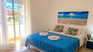 A bedroom with a bed, a painting of a beach, and a view through a sliding door. - Appartamenti Abate  Conchiglia Home  (Alcamo)