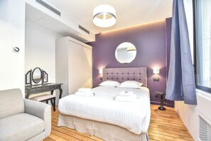A hotel room with a bed, a desk, a chair, a round mirror, and a window with curtains. - Residence Paris Helder (Paris)