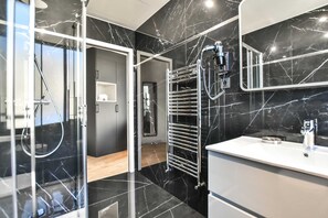 A modern bathroom with a black marble floor, a white sink, and a glass shower enclosure. - Residence Paris Helder (Paris)