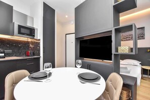 A modern kitchen with a microwave, toaster, and a coffee machine. There is a dining area with a round table, chairs, and a TV mounted on the wall. - Residence Paris Helder (Paris)