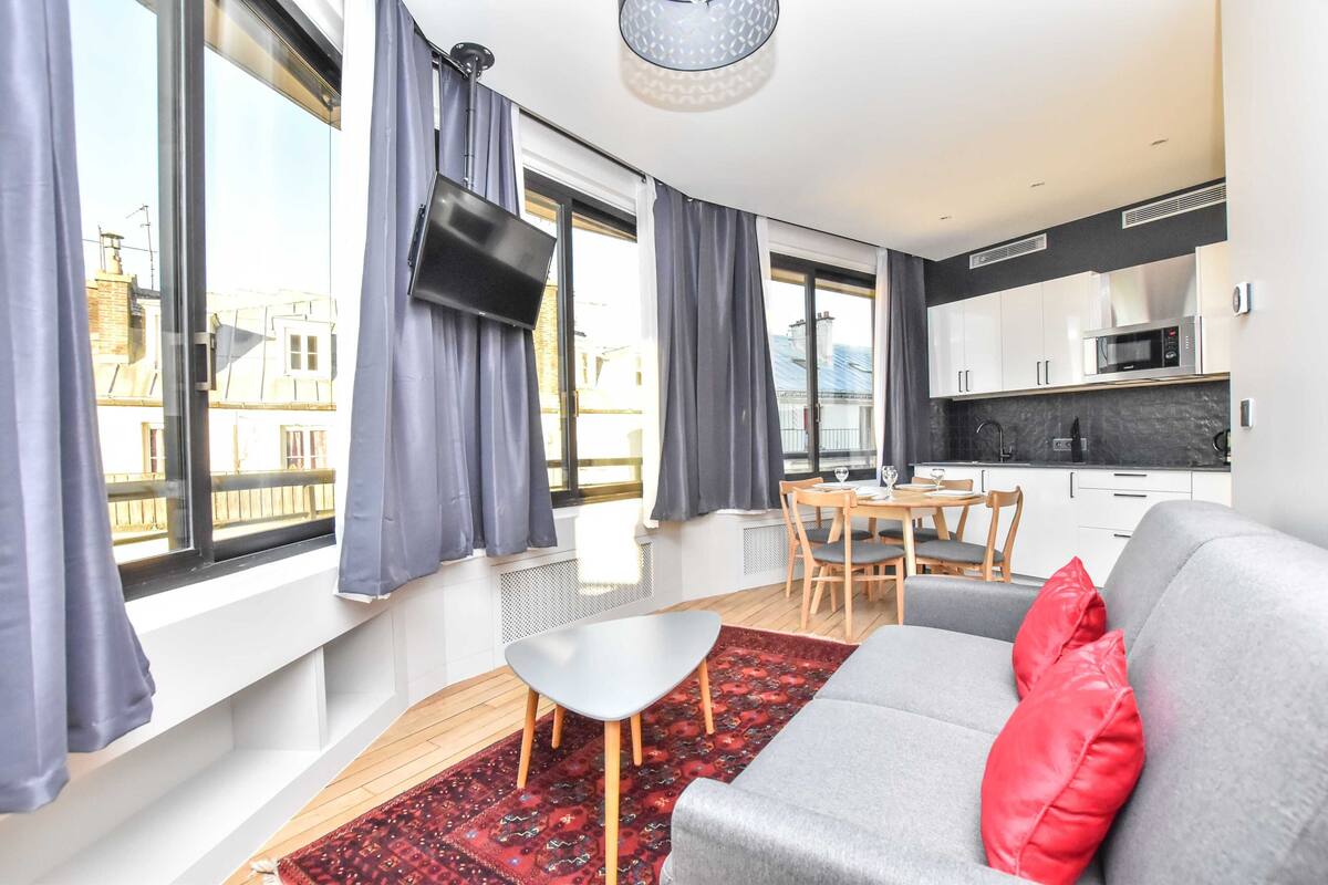 Ein modernes Apartment mit einem grauen Sofa, roten Kissen, einem kleinen Tisch und einem an der Wand befestigten Fernseher.