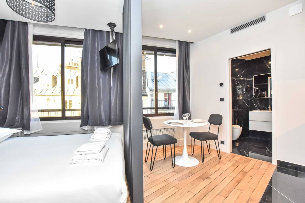 Ein Hotelzimmer mit Bett, einem runden Tisch mit Stühlen, einem Fernseher und einem Badezimmer mit Spiegel und Waschbecken.