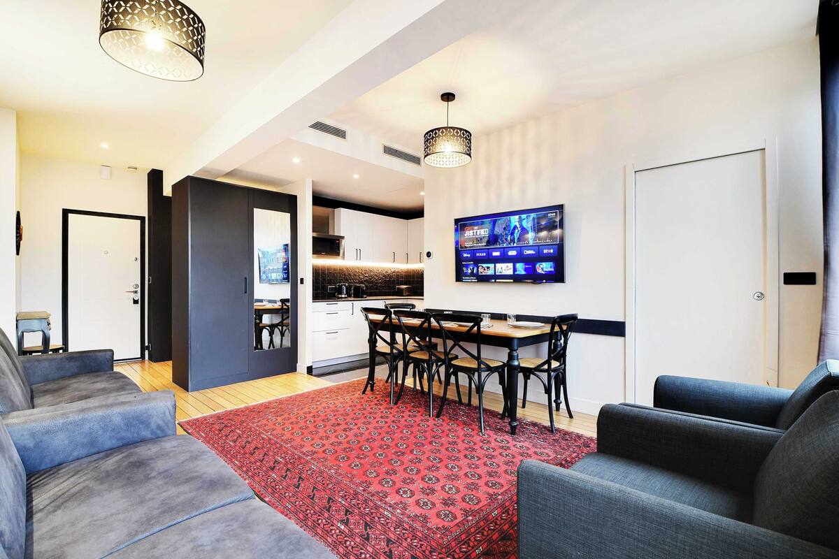 Ein modernes Wohnzimmer mit einem roten Teppich mit Muster, grauen Sofas und einem Essbereich mit einem Holztisch und Stühlen.