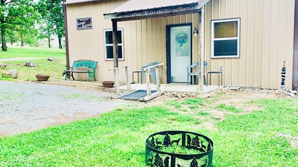 A small, single-story building with a covered porch, a sign indicating a retreat, and a metal fence with animal silhouettes. - Sweet Retreat (Mountain Home)