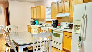 A kitchen with wooden cabinets, a white refrigerator, a dining table with chairs, and a microwave. - Sweet Retreat (Mountain Home)