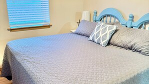 A neatly made bed with a blue quilt, a wooden floor, and a window with blinds. - Sweet Retreat (Mountain Home)