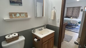 Une salle de bain comprenant des toilettes, un lavabo, un meuble-lavabo et un miroir avec éclairage. On y trouve également un porte-serviettes et un tableau encadré accroché au mur.
