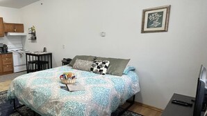 Une chambre comprenant un lit, un bureau, une chaise, un petit coin cuisine et un téléviseur.