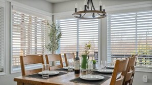 A dining area with a wooden table set for four, surrounded by chairs, with a chandelier above. - Epic Views, Hot Tub, Pets Welcome!  Overlooking Shenandoah National Park (Stanley)