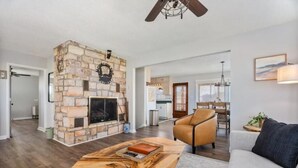 A spacious living room with a stone fireplace, a wooden coffee table, a leather sofa, and a dining area in the background. - Epic Views, Hot Tub, Pets Welcome!  Overlooking Shenandoah National Park (Stanley)