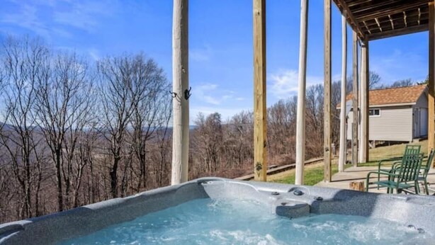 A hot tub with a wooden deck and a view of trees and a house in the background. - Epic Views, Hot Tub, Pets Welcome!  Overlooking Shenandoah National Park (Stanley)