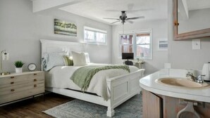 A bedroom with a bed, bedside table, dresser, and a bathroom with a sink and mirror. - Epic Views, Hot Tub, Pets Welcome!  Overlooking Shenandoah National Park (Stanley)