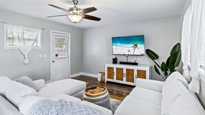 A modern living room with a ceiling fan, a large TV mounted on the wall, and a large plant. - Beachy getaway in lovely Lakeland, Fl!  (Lakeland)