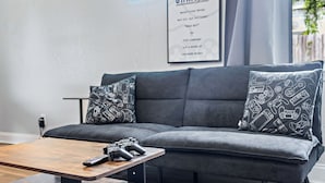 A modern living room with a grey sofa, two patterned pillows, and a coffee table with a remote control and game controller. - Beachy getaway in lovely Lakeland, Fl!  (Lakeland)